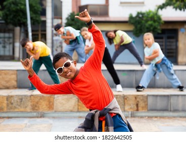 Portrait of confident african boy in sunglasses dancing hip-hop with group of tweens on summer city street.