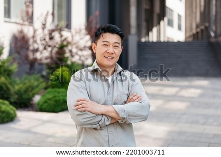 Portrait of confident asian entrepreneur posing with crossed arms and looking at camera near office building, outdoors. Ceo manager and boss, successful work