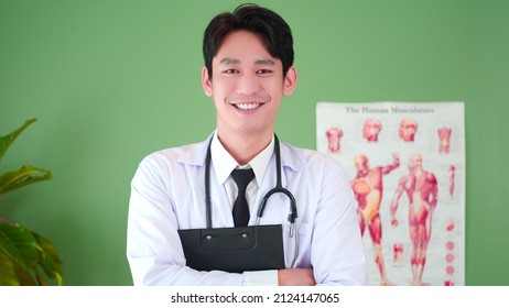 Portrait Of Confident Asian Young Male Physician Smile, Posing In Hospital Medical Office. Expertise, Professional Doctor In Uniform White Lab Coat Holding Clipboard Medical Records And Stethoscope.