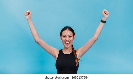 Portrait of confident beautiful asian fitness woman feeling happy and rise her hand up after exercise isolated on blue color background with copy space.Concept of slim and healthy girl workout.