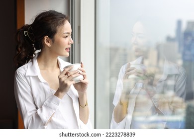 Portrait Of Confident And Beauty Young Asian Businesswoman With Coffee Cup Standing And Looking Away In Modern Hotel With City Blurred Background. Success Business And Lifestyle Concept