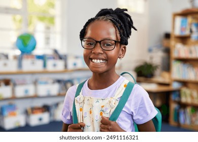 Portrait of a confident black girl wearing spectacles while holding backpack at library. Cheerful african american schoolgirl wearing eyeglasses standing in classroom while looking at camera.  - Powered by Shutterstock