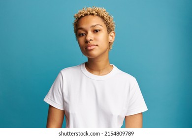 Portrait of confident blonde African American millennial woman with nose and ears pierced, wearing white t-shirt with copy space for your advertising content standing against blue studio wall - Shutterstock ID 2154809789
