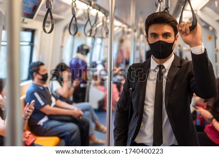 Portrait of confident businessman in black suit wear mask in city finding job during corona crisis using smartphone travelling on empty train