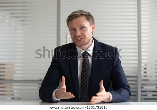 Portrait confident businessman coach wearing\
suit looking at camera and talking, making video call, mentor coach\
tutor recording webinar, online course, hr manager holding distance\
job interview