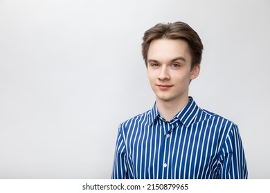 Portrait of confident and cheerful young man wearing blue-white striped button shirt looking at camera with one eyebrow raised. Studio shot on gray background