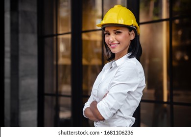 Portrait Of A Confident Construction Engineer Woman. Mixed Race Female Smiling And Looking At Camera. Standing In Front Of The Modern Office Building