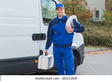 Portrait of confident electrician with cable coil and toolbox standing outside truck