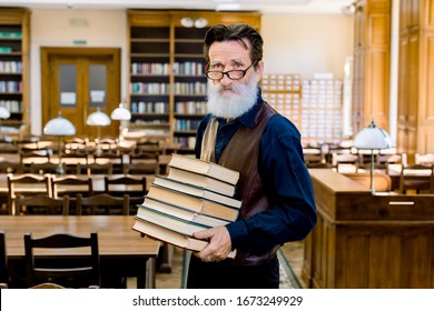 Portrait Of Confident Elegant Librarian Of University Professor Teacher Man, Wearing Stylish Clothes, Happy To Share Knowledge, Holding Stack Of Different Books, Standing In Vintage Library Indoors.