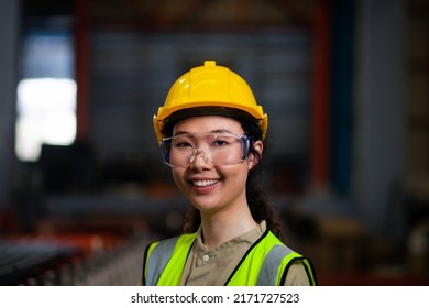 Portrait of a confident female Asian worker in a safety vest with a hard hat smiling at the camera in a sheet metal factory. Heavy industrial plants. female engineer in factory - Powered by Shutterstock