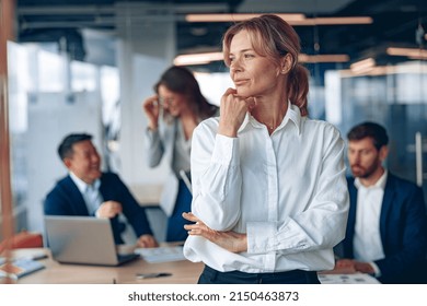 Portrait Of Confident Female Boss Looking At Side With Her Colleagues At Background In Office. 