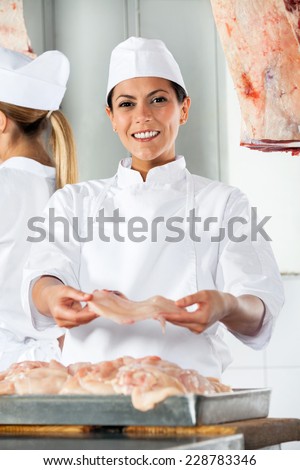 Portrait of confident female butcher offering raw meat in shop