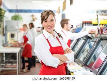 Portrait of confident female butcher standing arms crossed with colleagues in background - Powered by Shutterstock