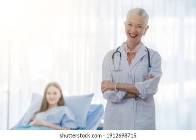 Portrait Of Confident Female Doctor With Stethoscope Wearing White Coat And Blurred A Patient Lying On Bed In Hospital