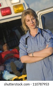 Portrait Of A Confident Female EMT Doctor Standing With Patient Lying On Stretcher In The Background