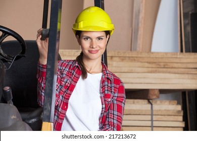 Portrait Of Confident Female Engineer Wearing Hardhat While Standing By Forklift In Workshop