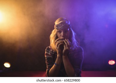 Portrait of confident female musician playing harmonica in illuminated nightclub - Powered by Shutterstock