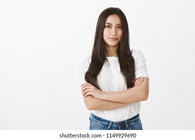 Portrait Of Confident Feminine European Girlfriend With Tanned Skin And Dark Hair, Holding Hands Crossed And Smiling With Self-assured Expression, Being Bossy During Meeting With Team