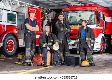 Portrait of confident firefighters with equipment against trucks at fire station