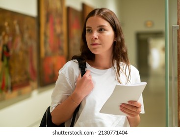 Portrait of a confident girl with an information booklet, standing in the hall of the historical museum next to the ..exhibit, located in a glass cabinet