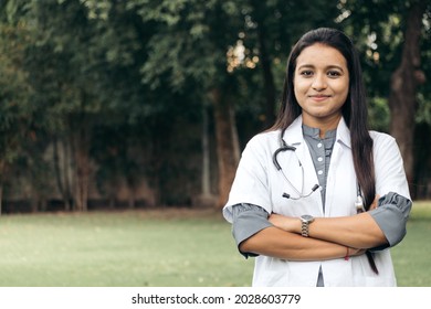 Portrait Of Confident Indian Doctor Wear White Coat, Standing At Outdoors With Arms Crossed On Chest. Professional Front Line Covid Warriors During Covid-19, Medical Service Concept. With Copy Space