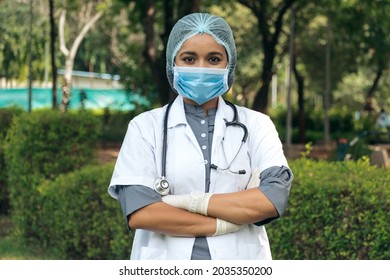 Portrait of confident Indian doctor wear white coat and mask standing at outdoors with arms crossed on chest. Professional occupation person during covid-19, concept of medical service In India