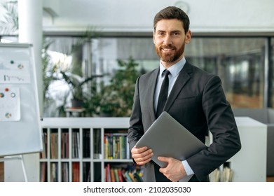 Portrait Confident Intelligent Proud Caucasian Businessman, Top Manager, Lawyer Or IT Specialist, In Shirt, Stands In Modern Office, Holding A Laptop, Looking At The Camera With A Friendly Smile