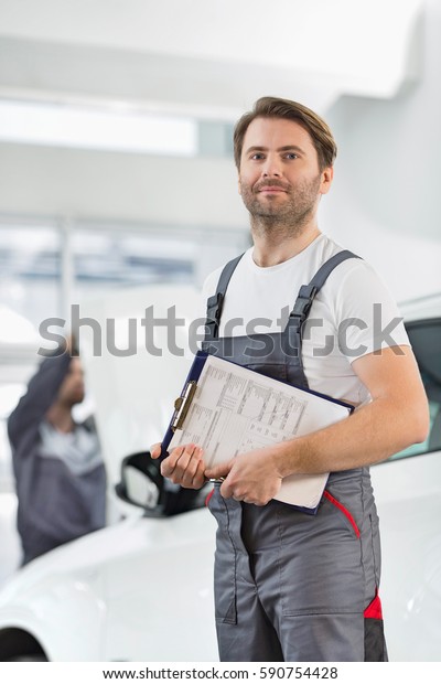 Portrait of confident male automobile mechanic with\
clipboard in car repair\
store