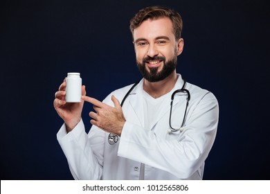 Portrait Of A Confident Male Doctor Dressed In Uniform With Stethoscope Pointing Finger At Bottle With Pills Isolated Over Dark Background