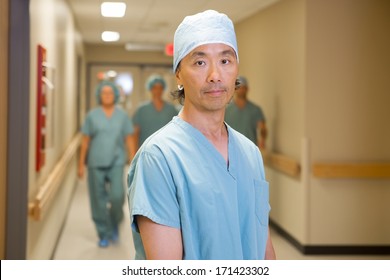 Portrait Of Confident Male Doctor With Team Walking In Hospital Corridor