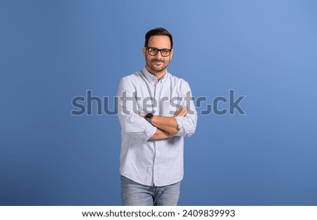 Portrait of confident male professional manager with arms crossed posing on isolated blue background