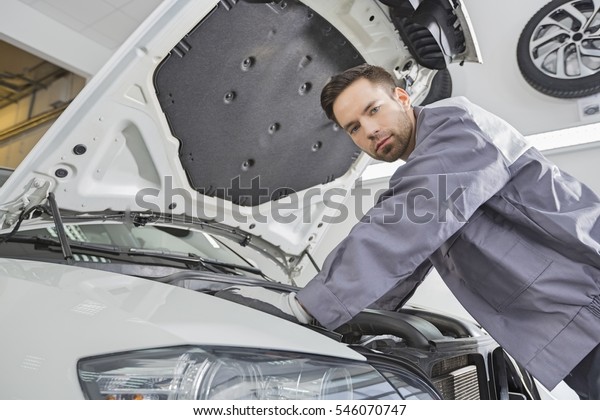 Portrait of confident male repair worker repairing\
car engine in repair\
shop