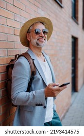 Portrait Of Confident Man Wearing Straw Hat And Backpack, Using Smartphone, Businessman In Casual Clothes In Summer On The Way To Work.