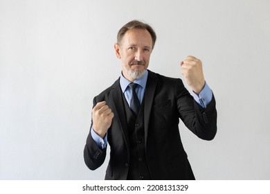 Portrait Of Confident Mature Businessman Fighting With Fists. Senior Caucasian Man Wearing Three Piece Suit Boxing Against White Background. Business Competition And Leadership Concept