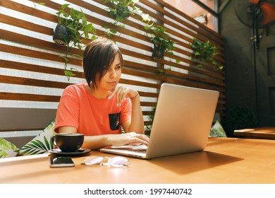 Portrait of confident mature professional woman sitting on summer terrace in cafe, using laptop computer for work, laughing happily indoors.  business woman in glasses, a coral T-shirt works from cafe - Powered by Shutterstock