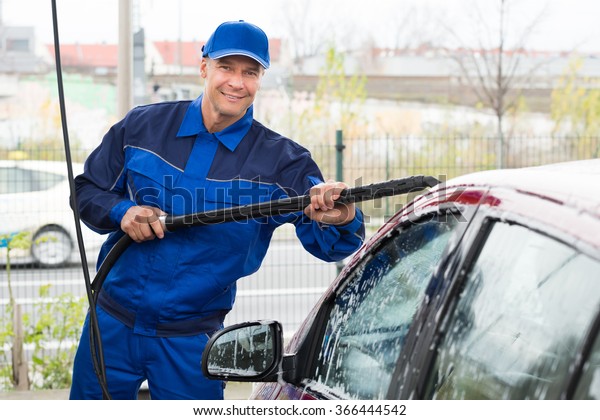 Portrait of confident mature serviceman washing\
car at garage