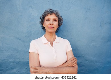 Portrait Of Confident Mature Woman Standing With Her Arms Crossed Against Blue Background