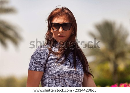 Portrait of confident middle aged woman in sportswear and sunglasses outdoors, looking at camera. Palm trees at backdrop. Healthy sports lifestyle and leisure activity concept. Copy text space for ad