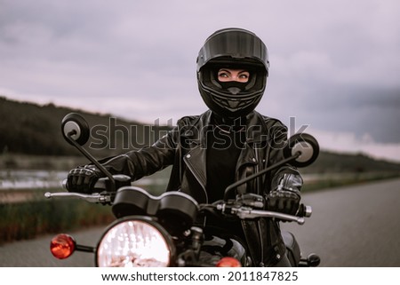 Portrait of confident motorcyclist woman in motorcycle helmet. Young driver biker looking away outdoors alone on highway. Ready for trip. Cafe racers, motorbike aesthetics and vintage design concept