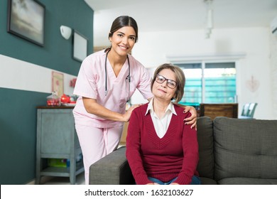 Portrait Of Confident Nurse By Elderly Woman Sitting On Sofa At Home