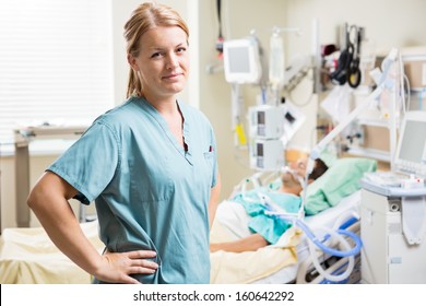 Portrait Of Confident Nurse Standing With Hand On Hip While Patient Resting In Background At Hospital