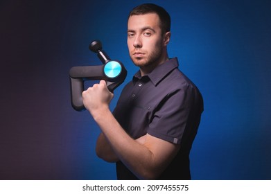 Portrait Of A Confident Professional Masseur With A Percussion Massager In His Hands. Low Key, Blue Background. Shock Wave Massage