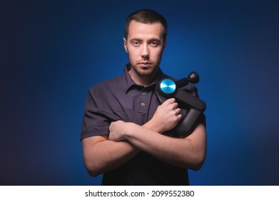 Portrait Of A Confident Professional Masseur With A Percussion Massager In His Hands. Low Key, Blue Background. Shock Wave Massage