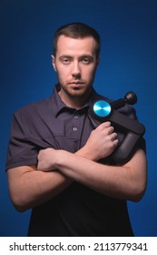 Portrait Of A Confident Professional Masseur With A Percussion Massager In His Hands. Low Key, Blue Background. Shock Wave Massage