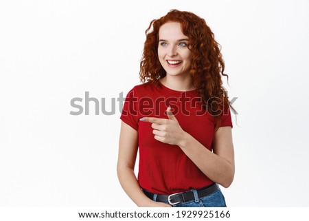 Portrait of confident redhead female student with curly long hair, pointing and looking left at banner logo, showing advertisement, white background