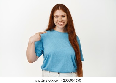 Portrait Of Confident Redhead Girl, Smiling White Teeth, Young Woman Pointing Finger At Herself, Talk About Her, Standing In Blue Tshirt Against White Background