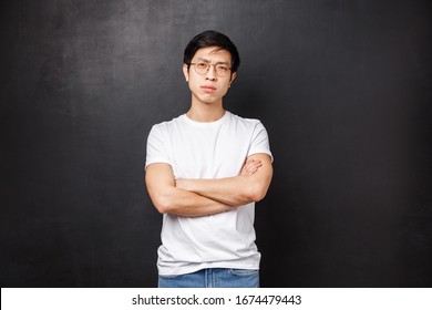 Portrait Of Confident Serious-looking Asian Macho Man In Glasses, Squinting Cautious And Looking Camera Disbelief, Cross Hands Over Chest, Do Not Trust Person Talking To, Black Background