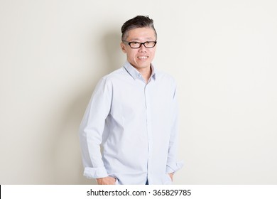 Portrait Of Confident Single Mature 50s Asian Man In Casual Business Arms Crossed And Smiling, Standing Over Plain Background With Shadow. Chinese Male People.