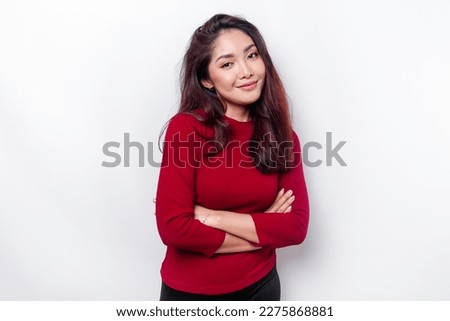 Portrait of a confident smiling Asian woman dressed in red, standing with arms folded and looking at the camera isolated over white background