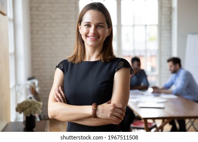 Portrait Of Confident Smiling Attractive Female Team Leader In Formal Dress Standing In Modern Workplace. Happy Young 30s Businesswoman Boss Employer Partner Posing Indoors, Looking At Camera.